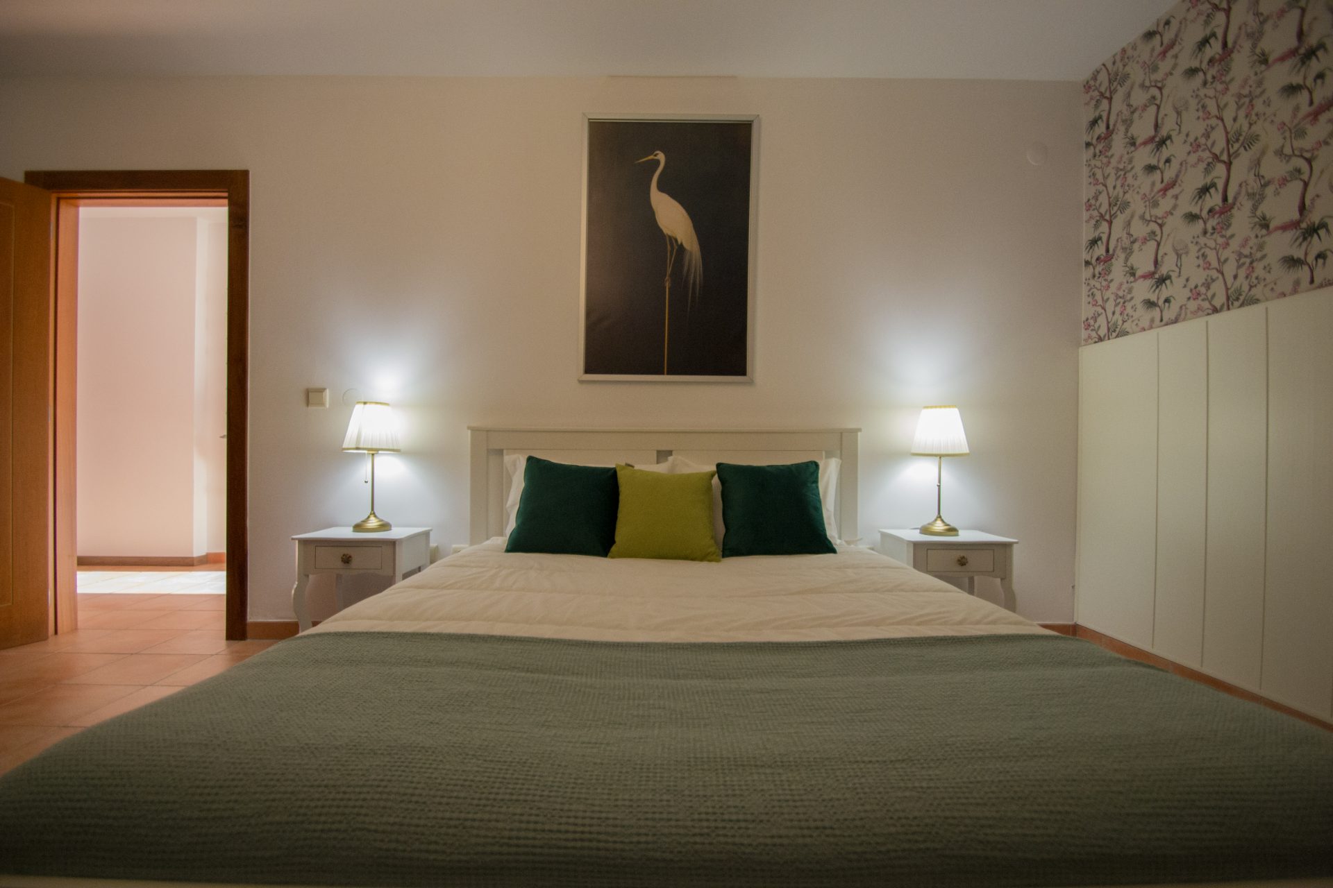 Quarto principal da Casa dos Grous com cama de casal, quadro de grou e papel de parede floral