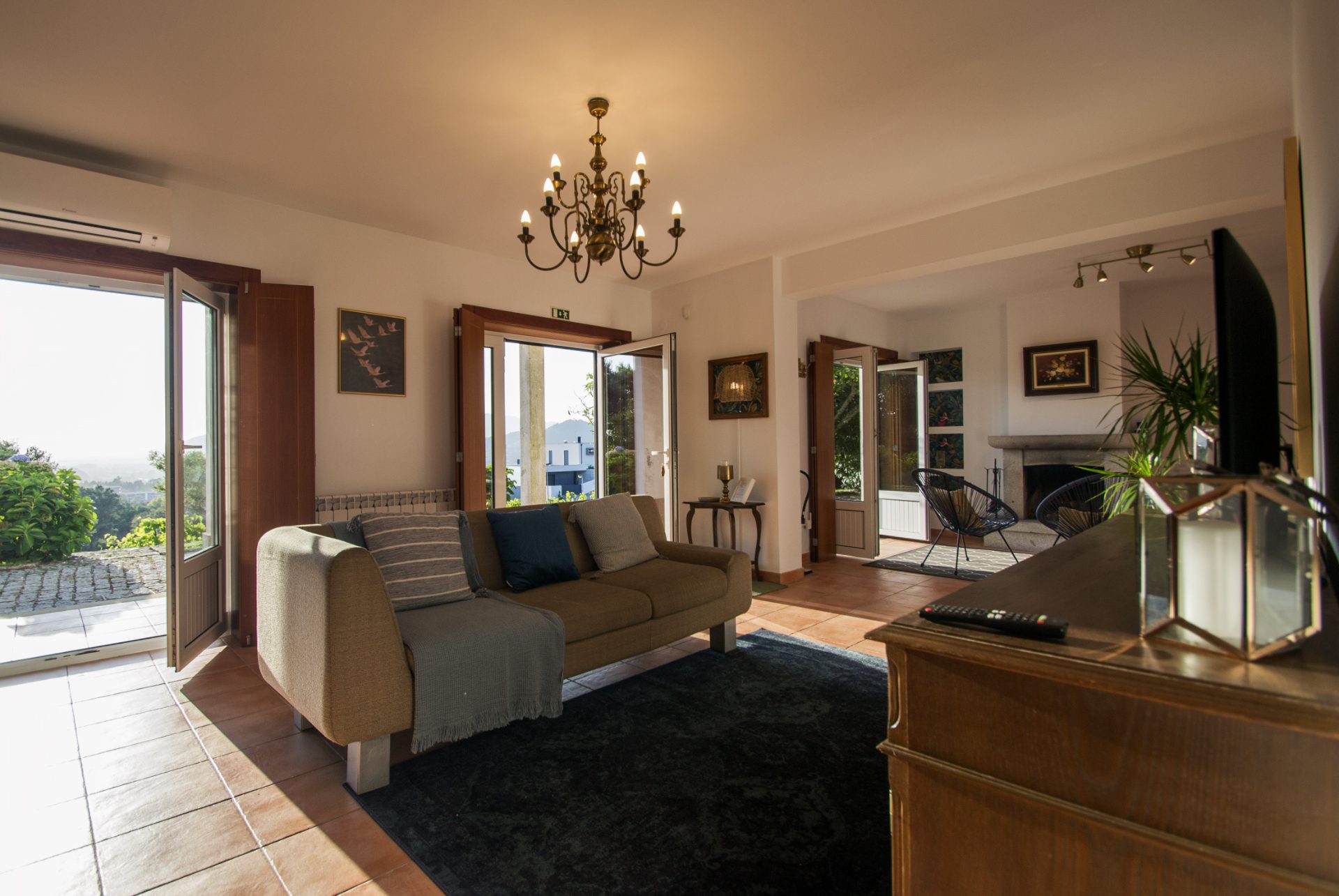 Sala de estar com sofá, candelabro de latão e portas abertas para o vale