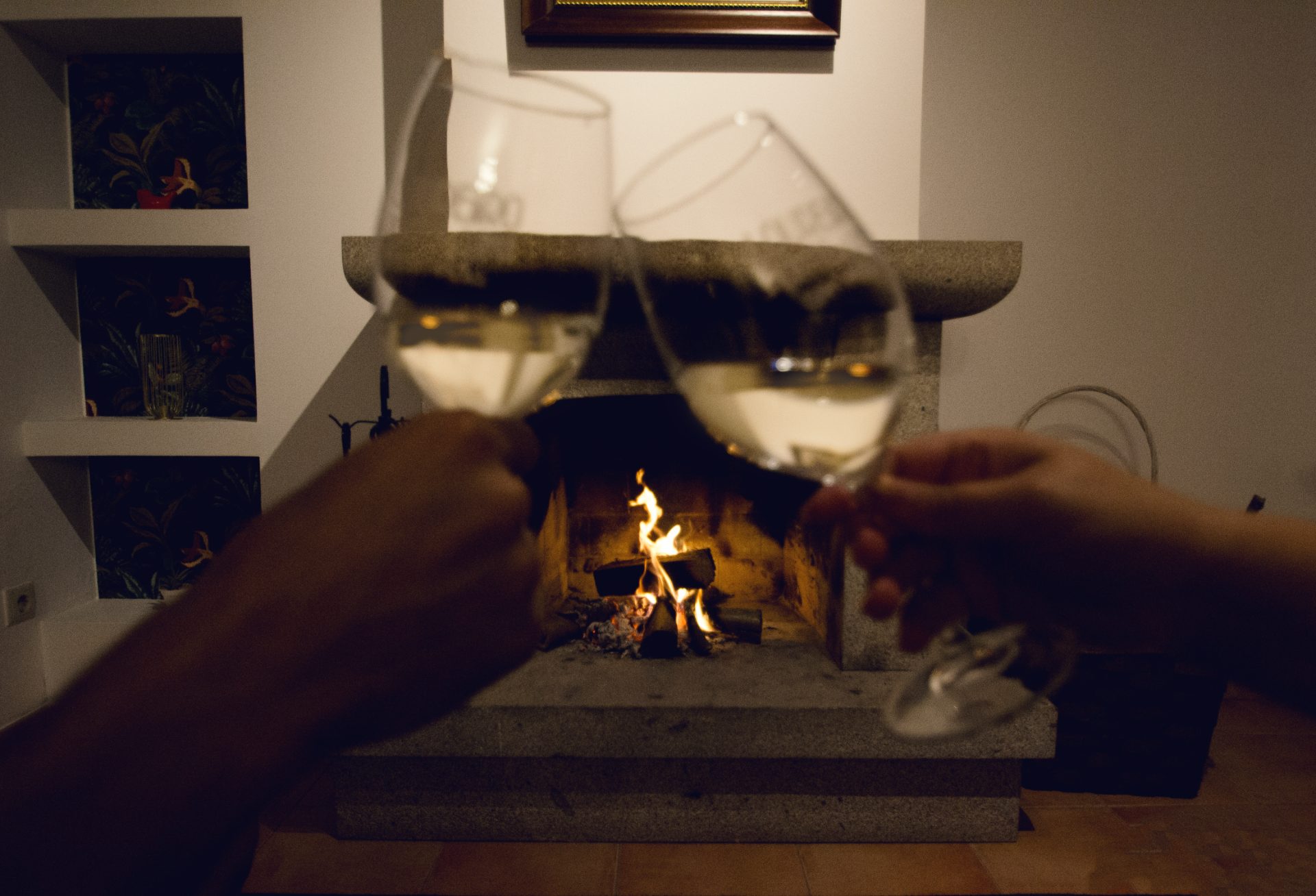 Dois copos de vinho verde brindados diante da lareira acesa