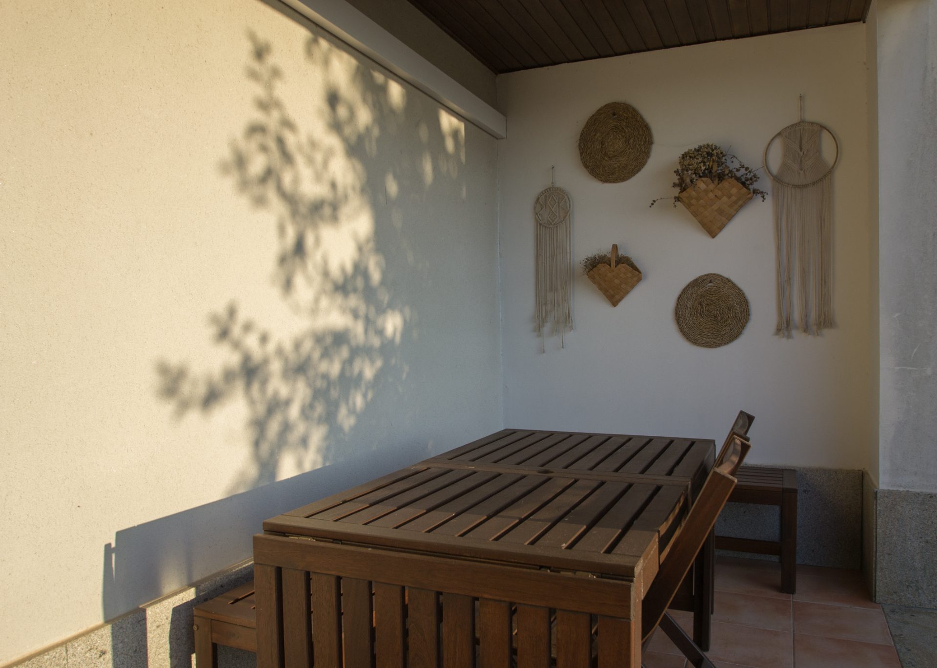 Terraço coberto com mesa de madeira e peças de cestaria na parede