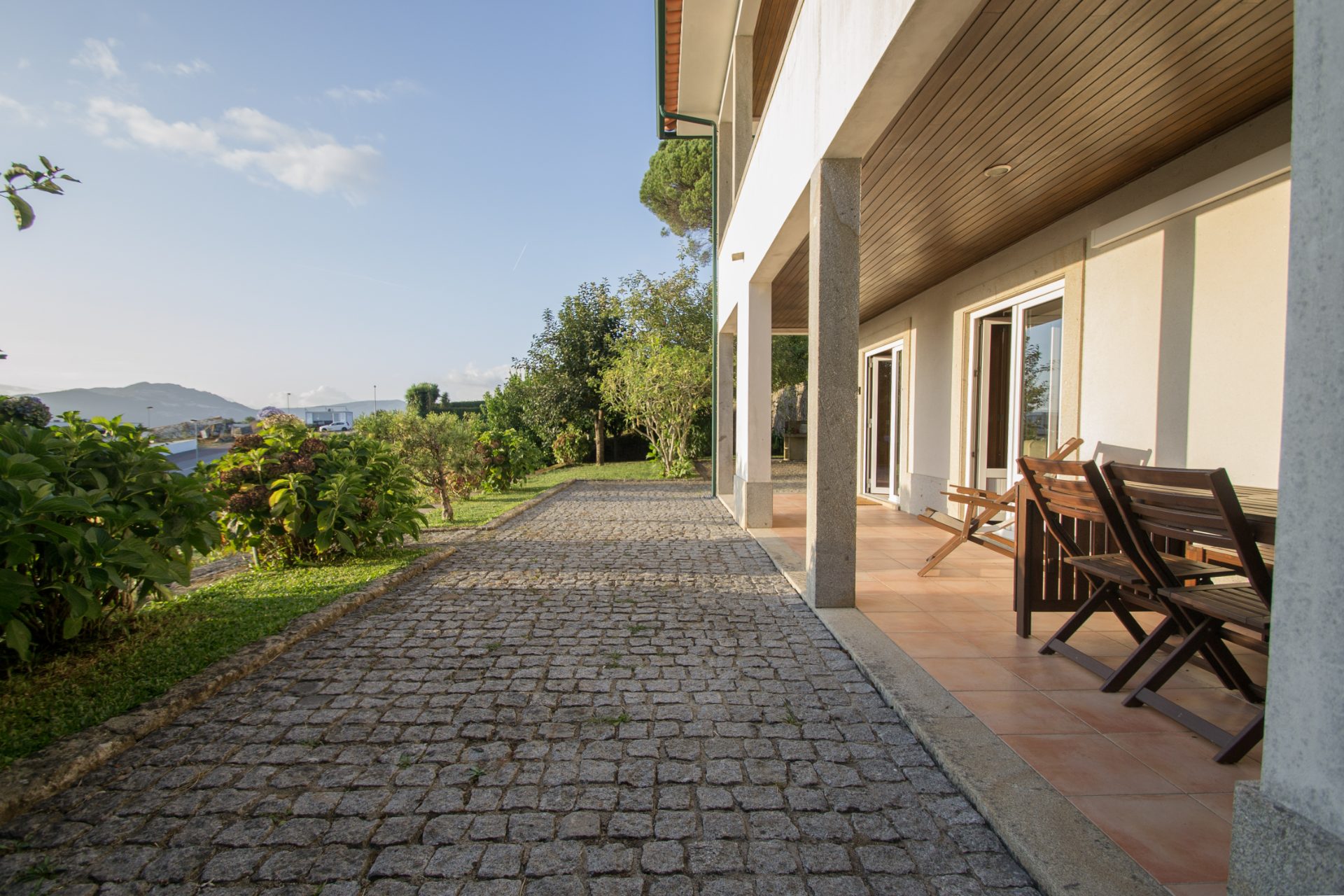 Alpendre exterior com cadeiras de madeira e caminho de cubos de granito